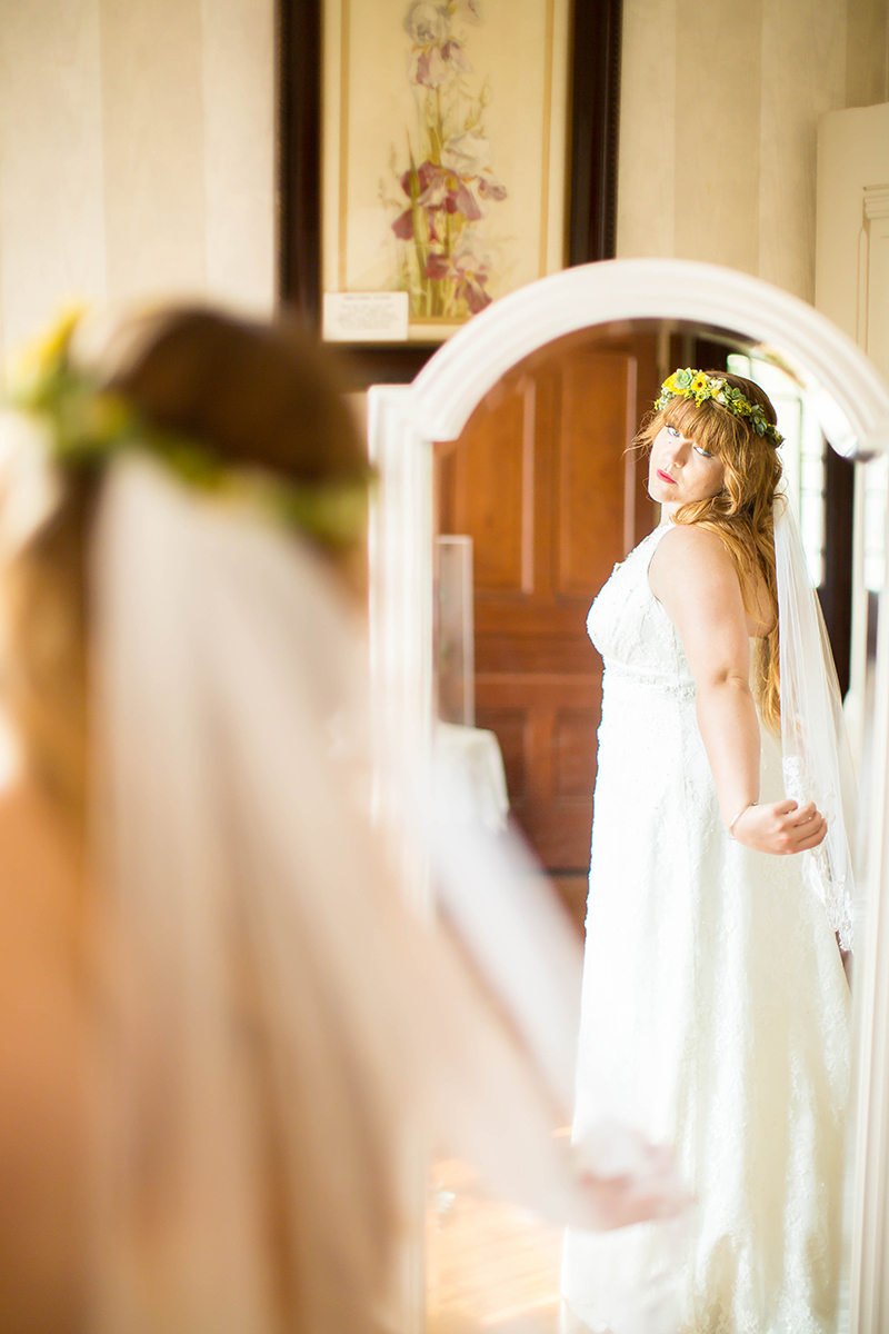 A bride looking in the mirror wearing a flower crown and white dress for this Camarillo Ranch wedding photography session