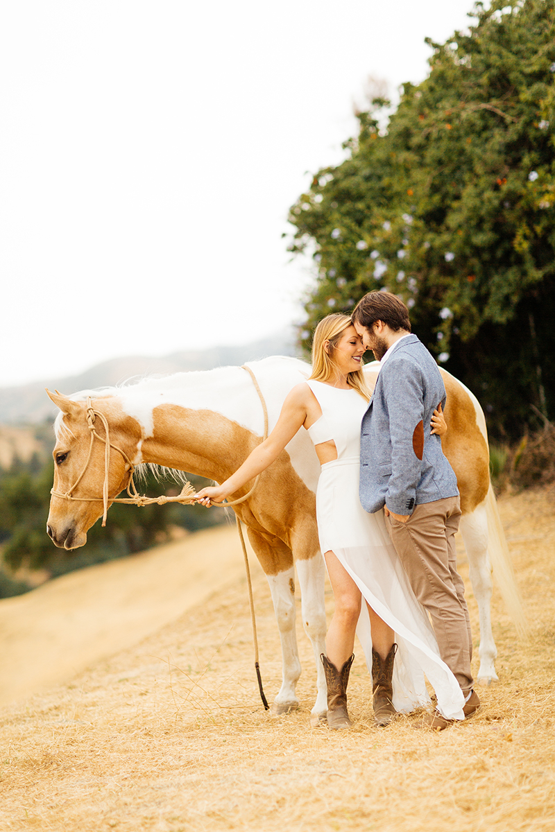 An engaged couple hold each other close with a horse on the hillside for this Granada Hills engagement photography session