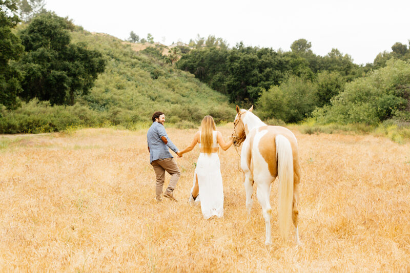 An engaged couple walk together with their horse on the hillside for this Granada Hills engagement photography session