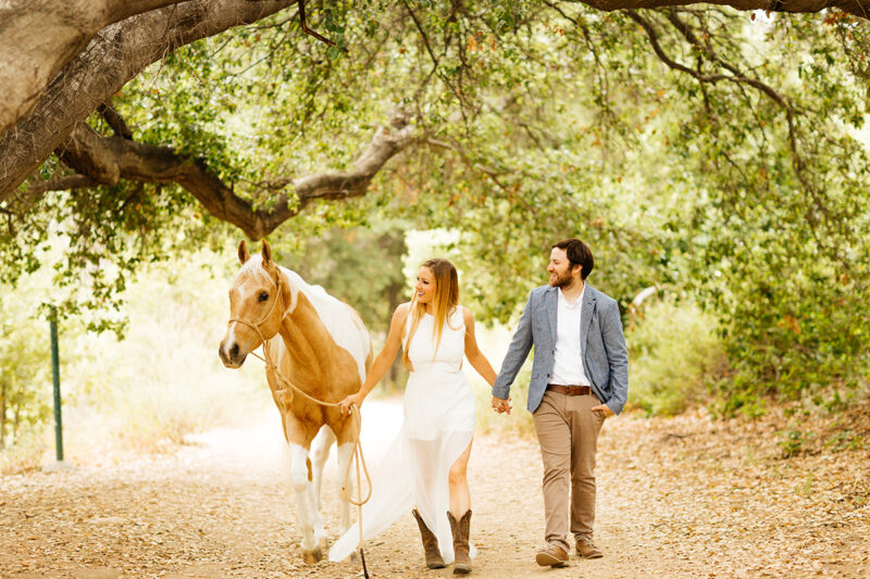 An engaged couple walk together with their horse on a trail for this Granada Hills engagement photography session