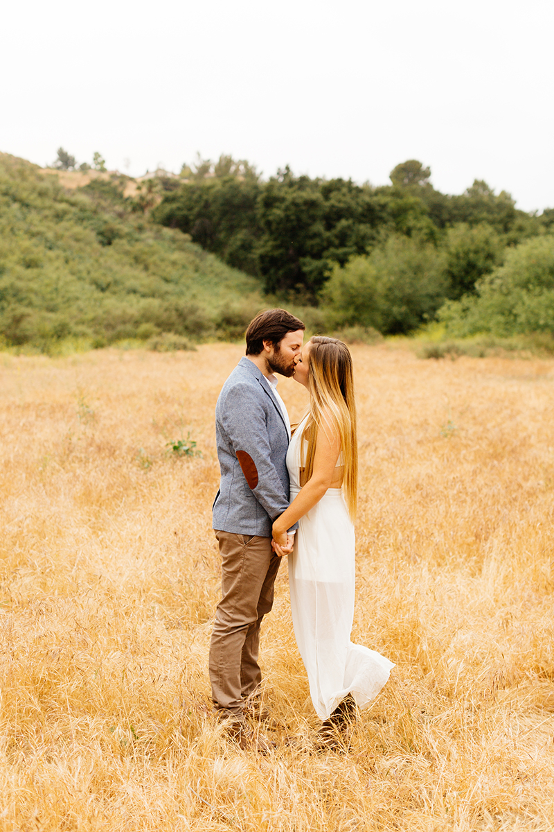 An engaged holding each other's hands kissing in a field for this Granada Hills engagement photography session