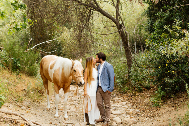 An engaged couple kiss holding each other with their horse on a trail for this Granada Hills engagement photography session