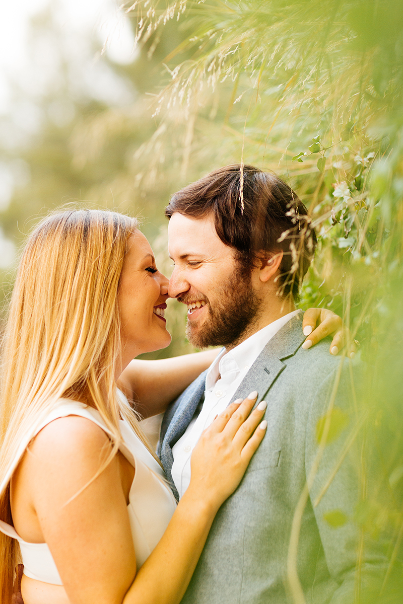 An engaged couple hold each other close leaning on a wall covered in plants for this Granada Hills engagement photography session