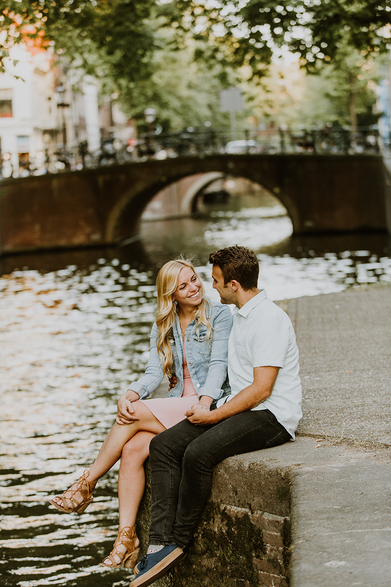 A couple sit together on the edge of a canal for this Amsterdam couples photography session