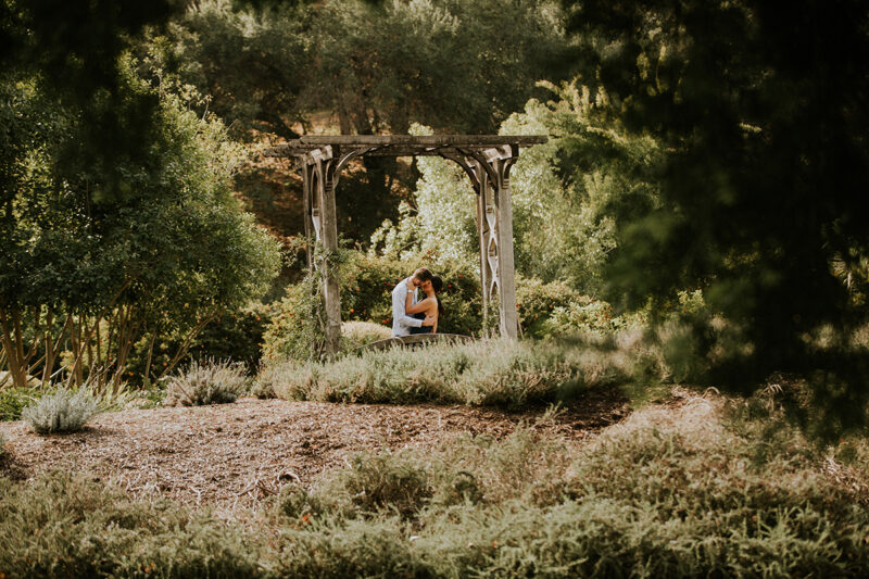 A couple hold each other and kiss at an arch at the Los Angeles County Arboretum and Botanic Garden for this Los Angeles engagement photography session