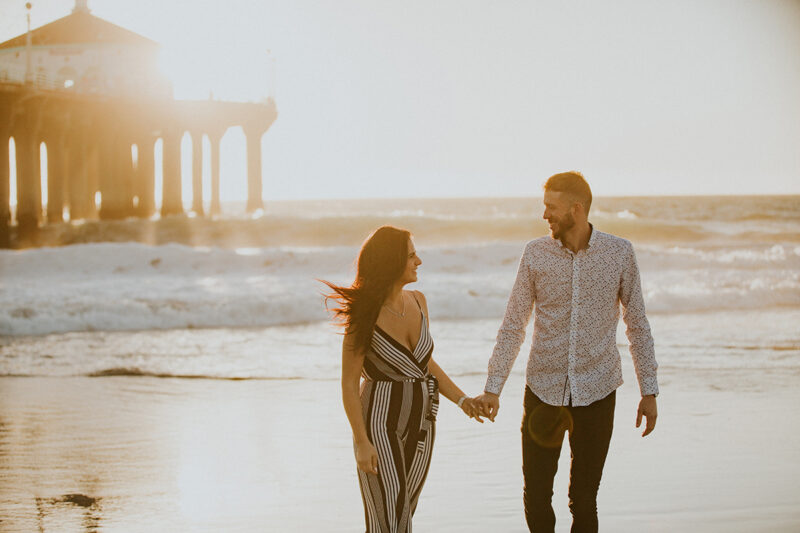 A couple walk together at sunset on the beach near the Santa Monica Pier for this Los Angeles engagement photography session