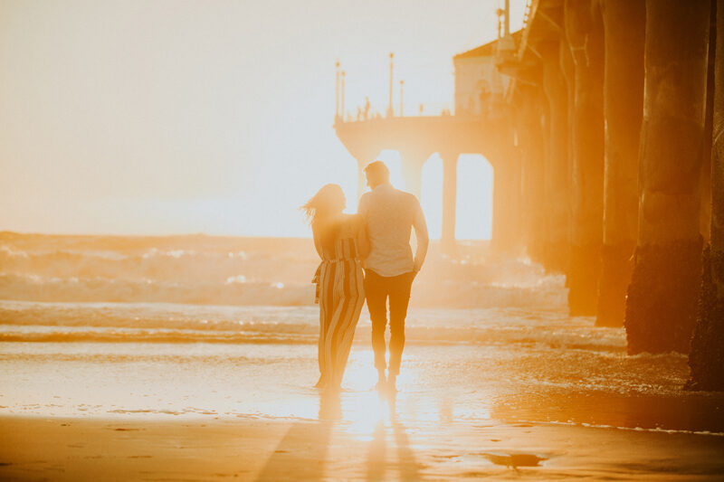 A couple walk together at sunset on the beach near the Santa Monica Pier for this Los Angeles engagement photography session