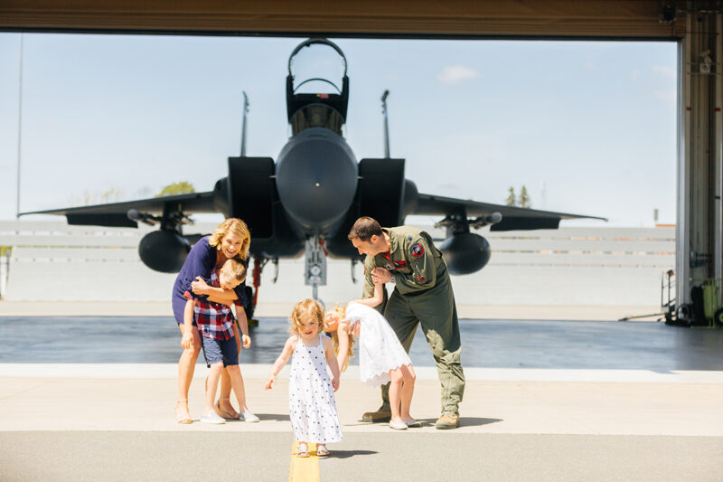 A family stands holding each other close in front of an F-15 fighter at Barnes Air National Guard Base near Boston wearing a flight suit and coordinated outfits for these F-15 fighter pilot family photos