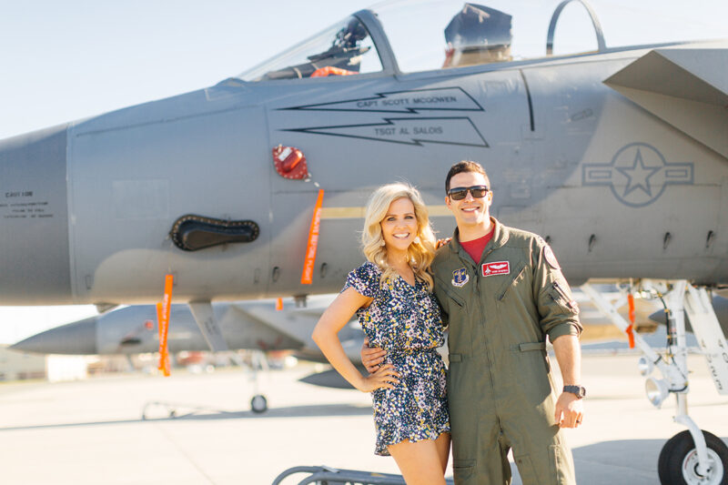 A pilot holds his wife in front of an F-15 at Barnes Air National Guard Base wearing a flight suit and a coordinated outfit for these F-15 fighter pilot family photos