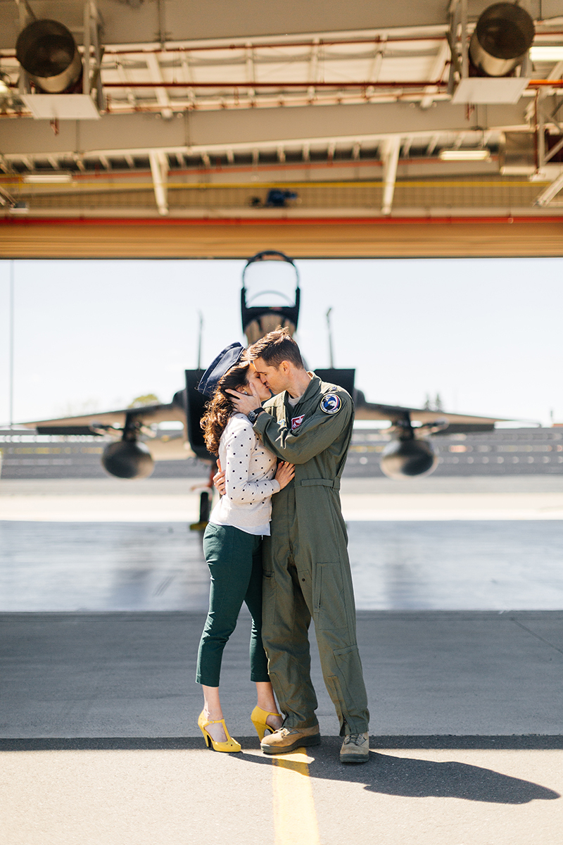 A pilot and his wife stand together kissing in front an F-15 at Barnes Air National Guard Base wearing a flight suit and a coordinated outfit for these F-15 fighter pilot family photos