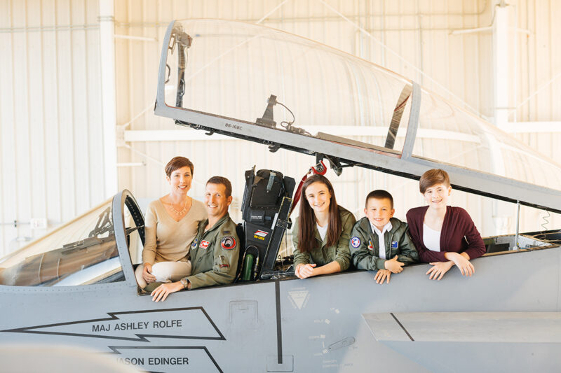 A family sits in the cockpit of an F-15 at Barnes Air National Guard Base wearing a flight suit and coordinated outfits for these F-15 fighter pilot family photos