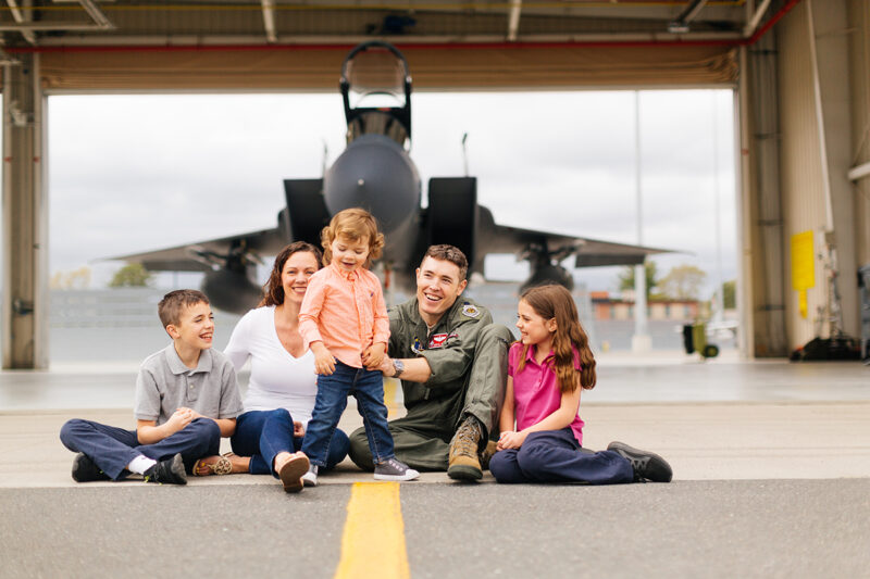 A family sits holding each other close in front of an F-15 at Barnes Air National Guard Base wearing a flight suit and coordinated outfits for these F-15 fighter pilot family photos
