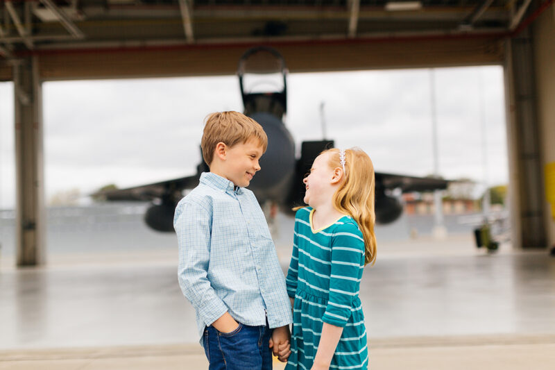 A pilot's children hold hands in front of an F-15 at Barnes Air National Guard Base wearing coordinated outfits for these F-15 fighter pilot family photos