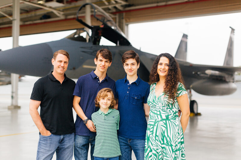 A family stands holding each other close in front of an F-15 at Barnes Air National Guard Base wearing coordinated outfits for these F-15 fighter pilot family photos
