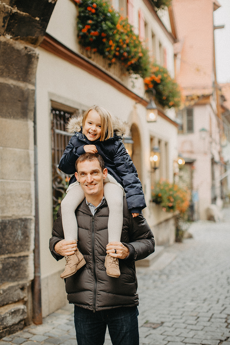 A father carries his daughter on his shoulders in Germany wearing coordinated outfits for a Rothenburg ob der Tauber family photography session