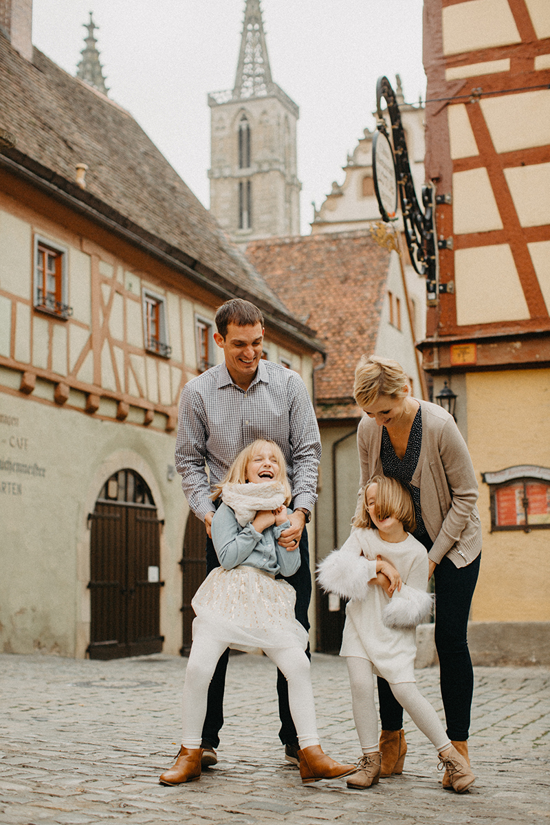 A family poses together laughing during a tickle fight in Germany wearing coordinated outfits for a Rothenburg ob der Tauber family photography session