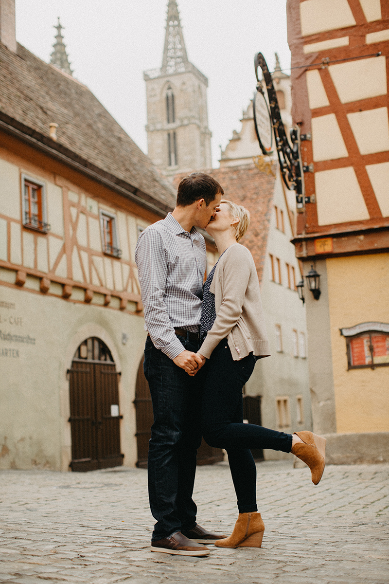 A couple hold hands and kiss in Germany wearing coordinated outfits for a Rothenburg ob der Tauber family photography session