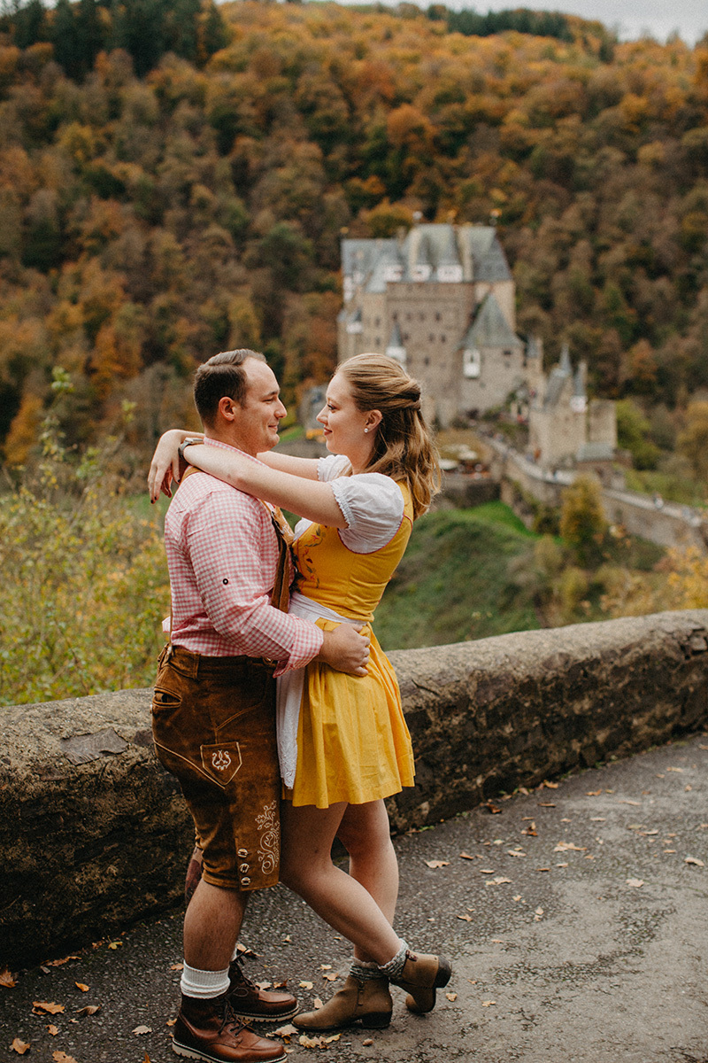 A couple hold one another on the road to Burg Eltz wearing a traditional dirndl and lederhosen for these Eltz Castle couples photos in Germany