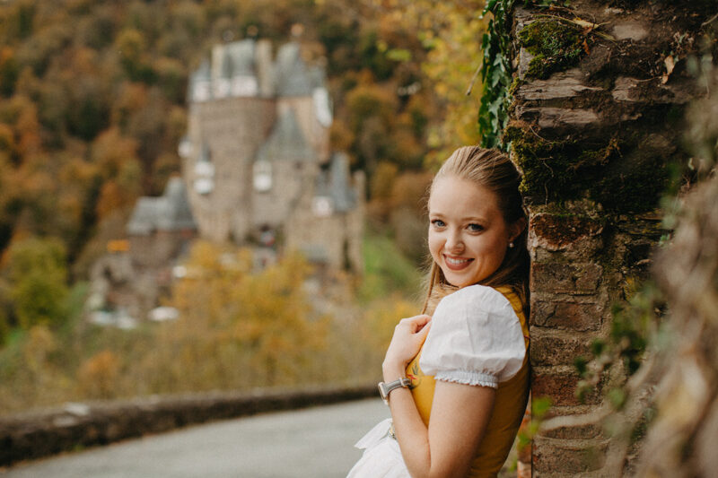 A beautiful young blonde woman poses on the road to Burg Eltz wearing a traditional dirndl for these Eltz Castle couples photos in Germany