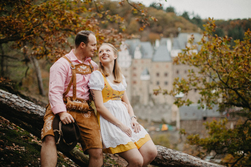 A couple embrace as they sit near Burg Eltz wearing a traditional dirndl and lederhosen for these Eltz Castle couples photos in Germany