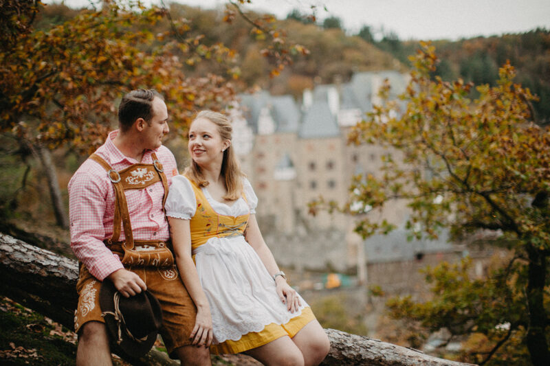 A couple embrace as they sit near Burg Eltz wearing a traditional dirndl and lederhosen for these Eltz Castle couples photos in Germany