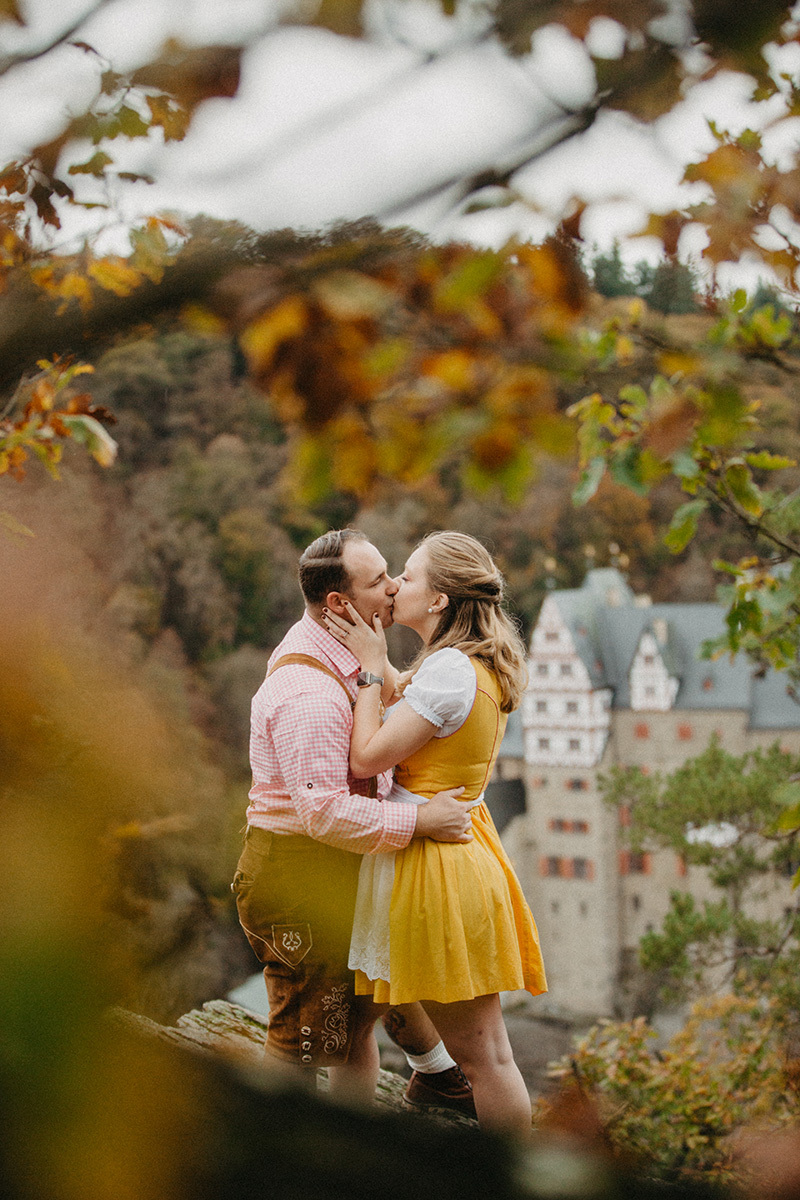 A couple embrace and kiss near Burg Eltz wearing a traditional dirndl and lederhosen for these Eltz Castle couples photos in Germany
