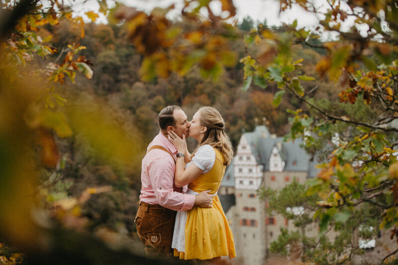 A couple embrace and kiss near Burg Eltz wearing a traditional dirndl and lederhosen for these Eltz Castle couples photos in Germany