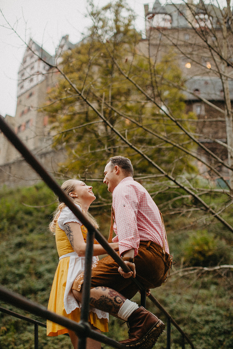 A couple embraces on a bridge near Burg Eltz wearing a traditional dirndl and lederhosen for these Eltz Castle couples photos in Germany