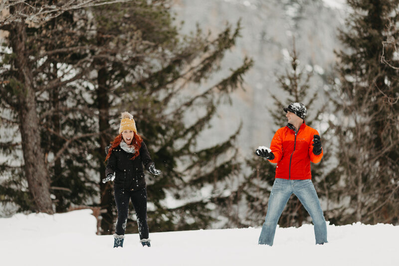 A couple having a snowball fight in trees on a snow covered mountain in Switzerland wearing snow gear for a Mürren couples photography session