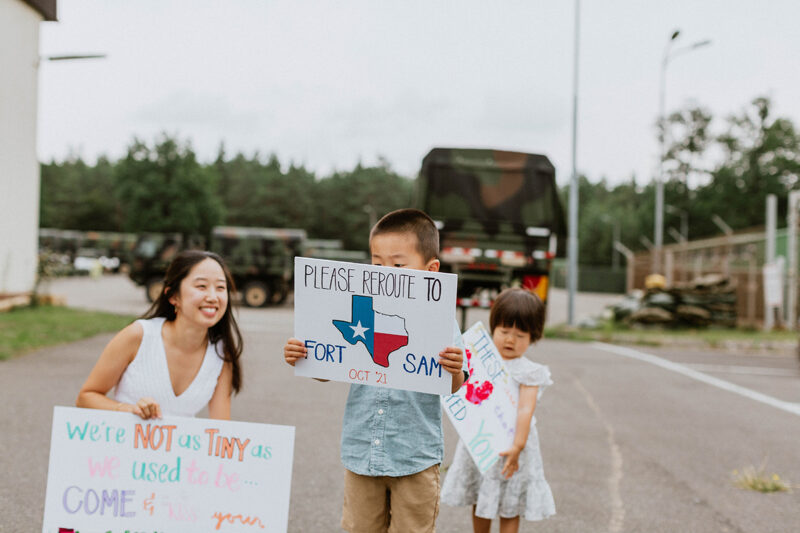 A family holds welcome home signs at the Rhineland Ordnance Barracks for Kaiserslautern homecoming photos in Germany