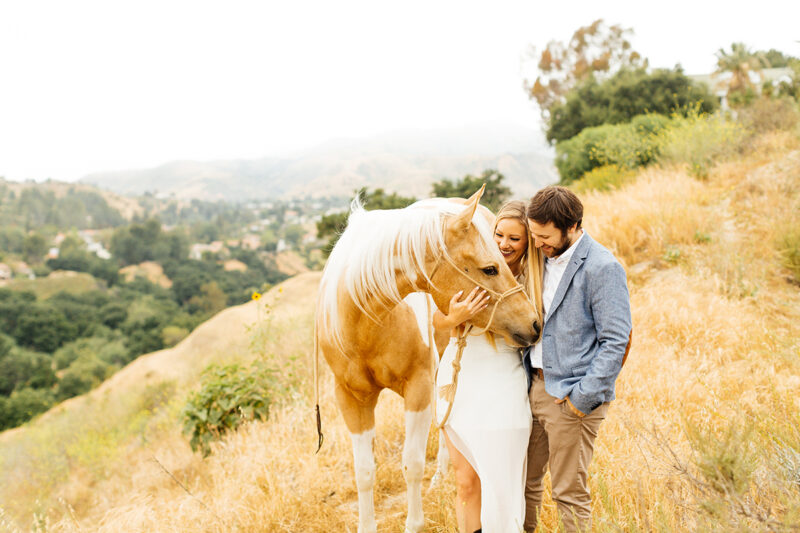 An engaged couple hold each other with their horse on the hillside for this Granada Hills engagement photography session