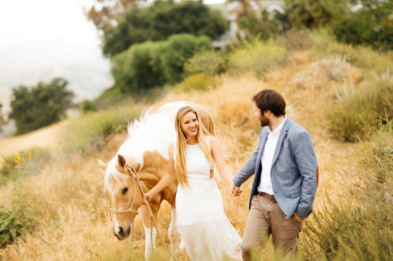 An engaged couple walk together with their horse on the hillside for this Granada Hills engagement photography session