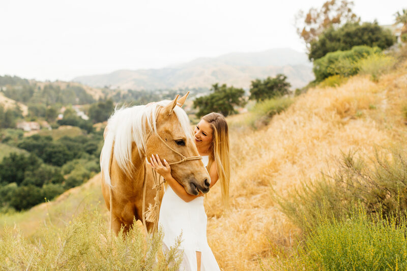 A woman pets her horse on the hillside for this Granada Hills engagement photography session