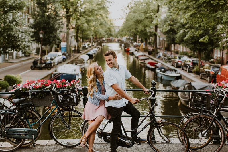 A couple sit on a bike on a bridge over a canal for this Amsterdam couples photography session