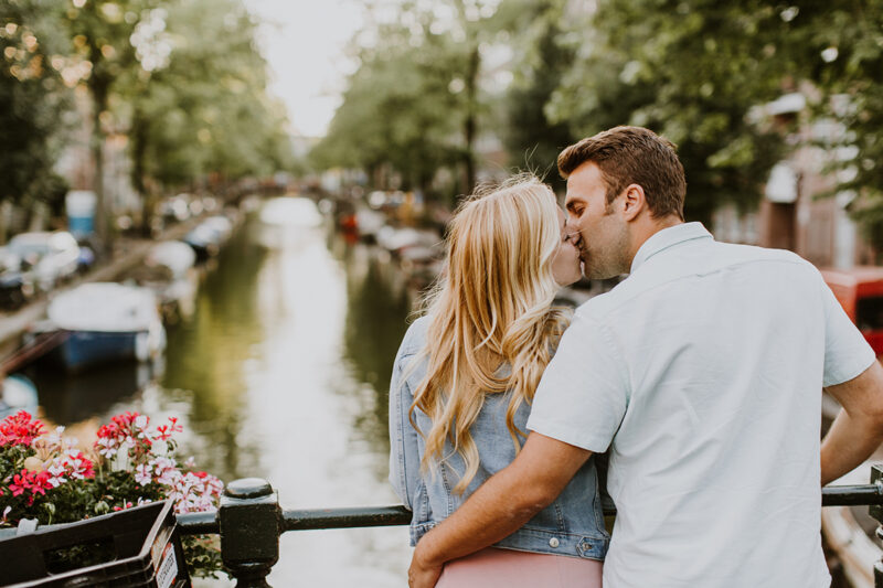 A couple hold one another close and kiss on a bridge over a canal for this Amsterdam couples photography session