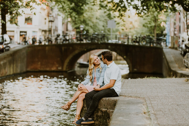 A couple sit together on the edge of a canal for this Amsterdam couples photography session