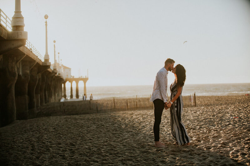 A couple kiss at sunset on the beach near the Santa Monica Pier for this Los Angeles engagement photography session