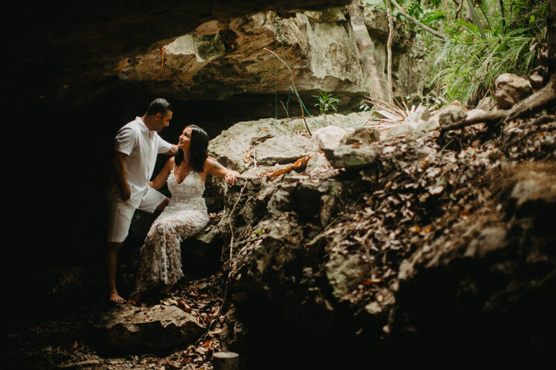 A couple together inside of a cenote in Mexico wearing a beautiful white dress and white shorts with a shirt for a Cenote Azul engagement photography session