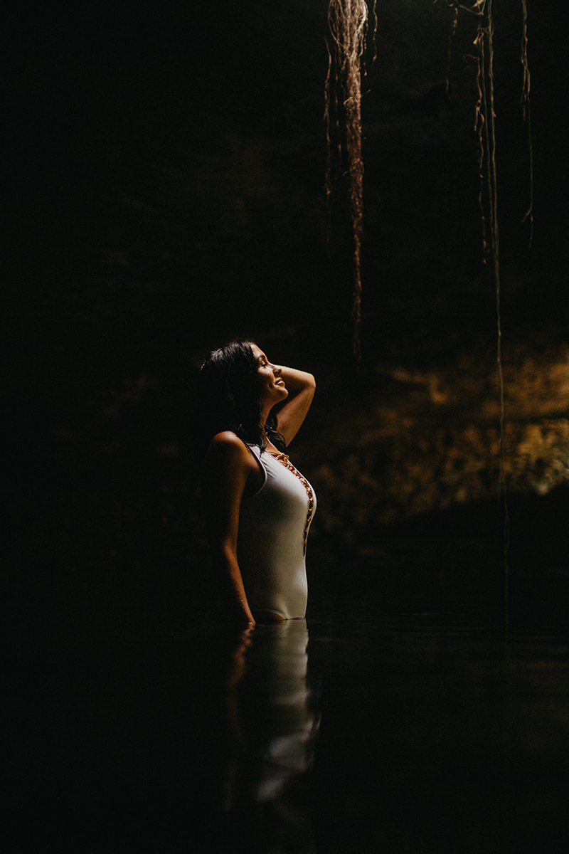 A beautiful woman poses in the water of a cenote in Mexico wearing a white swimsuit for a Cenote Azul engagement photography session