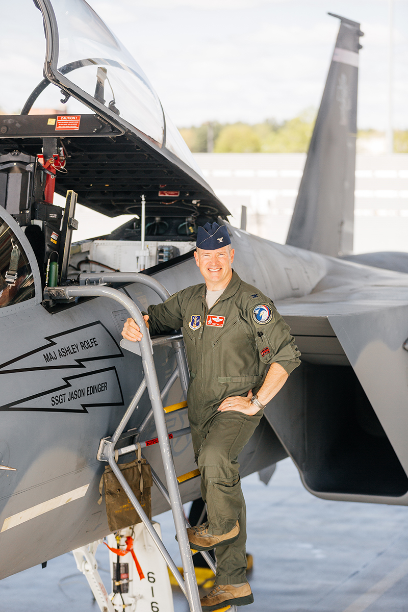 A pilot stands on a ladder up to an F-15 at Barnes Air National Guard Base wearing a flight suit for these F-15 fighter pilot family photos
