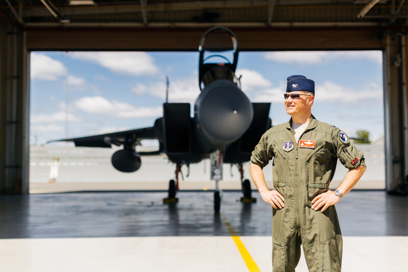 A pilot poses in front of an F-15 at Barnes Air National Guard Base wearing a flight suit for these F-15 fighter pilot family photos