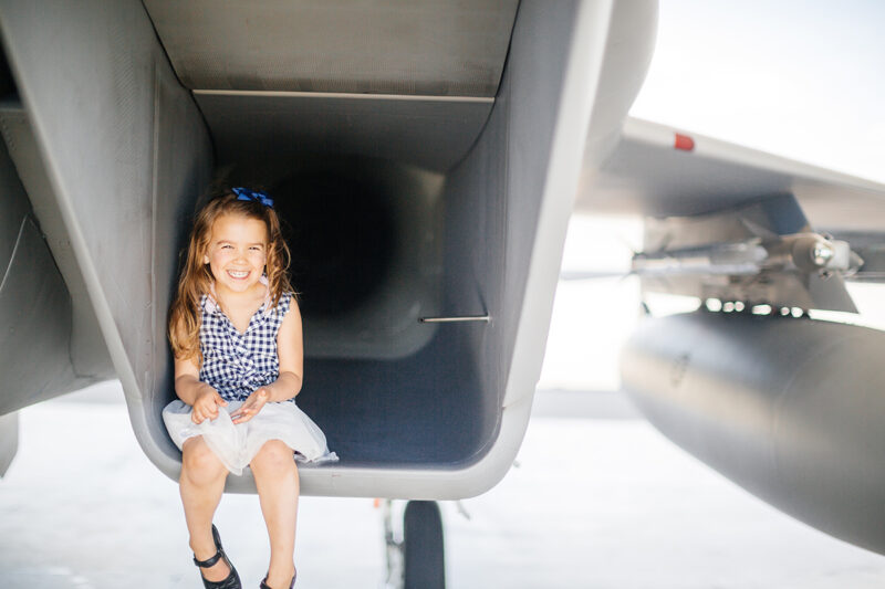 A girl sits in the intake of an F-15 at Barnes Air National Guard Base wearing a dress for these F-15 fighter pilot family photos