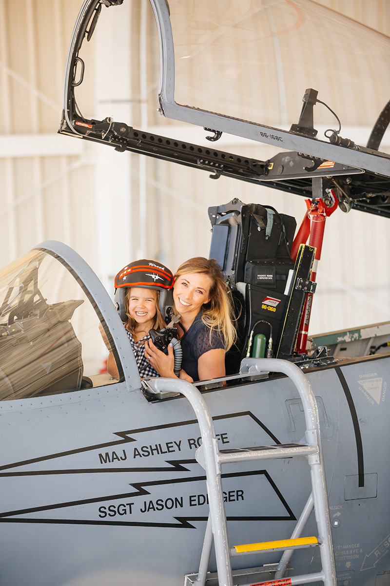A pilot poses in the cockpit of an F-15 with her daughter sitting on her lap at Barnes Air National Guard Base wearing coordinated outfits for these F-15 fighter pilot family photos