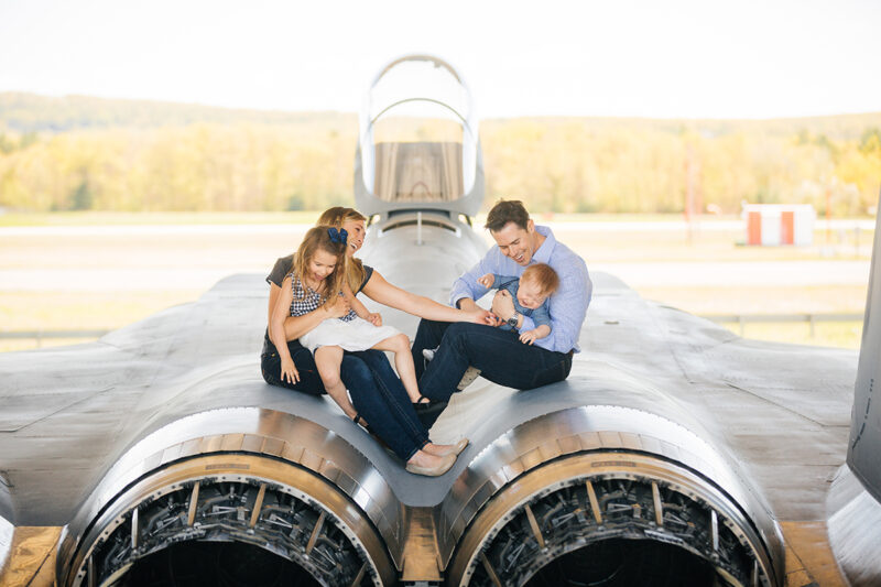 A family sits on an F-15 tickling one another at Barnes Air National Guard Base near Boston wearing coordinated outfits for these F-15 fighter pilot family photos