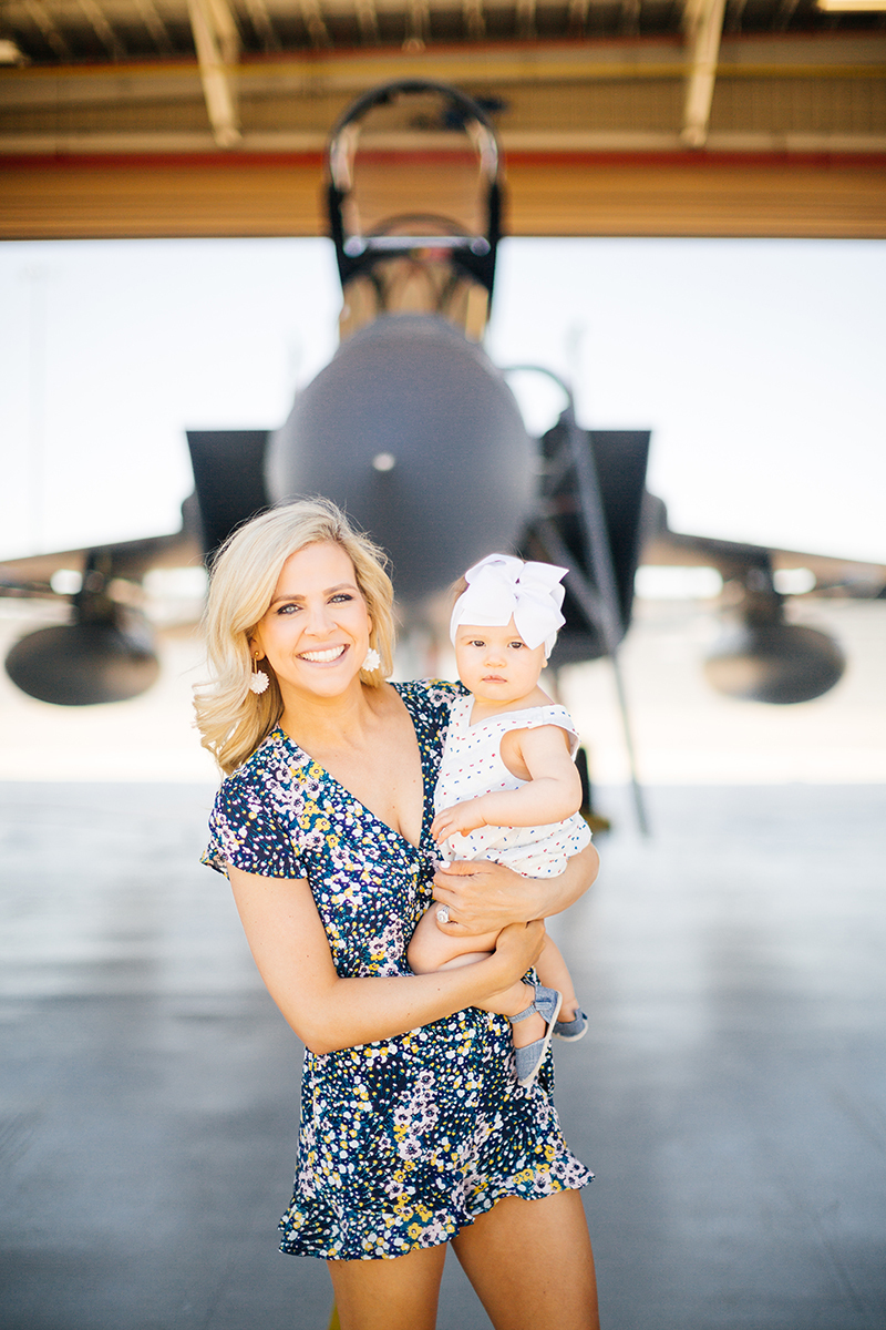 A pilot's wife holds their daughter in front of an F-15 at Barnes Air National Guard Base wearing coordinated outfits for these F-15 fighter pilot family photos