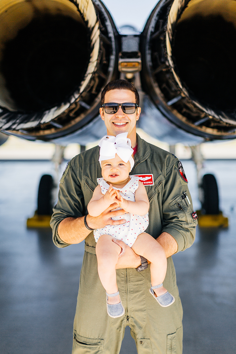 A pilot holds his daughter behind an F-15 at Barnes Air National Guard Base wearing a flight suit and a coordinated outfit for these F-15 fighter pilot family photos