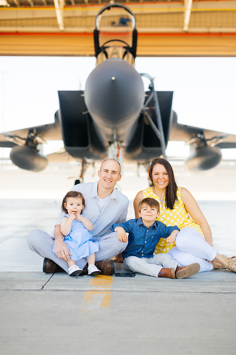 A family sits holding each other close in front of an F-15 at Barnes Air National Guard Base wearing a flight suit and coordinated outfits for these F-15 fighter pilot family photos