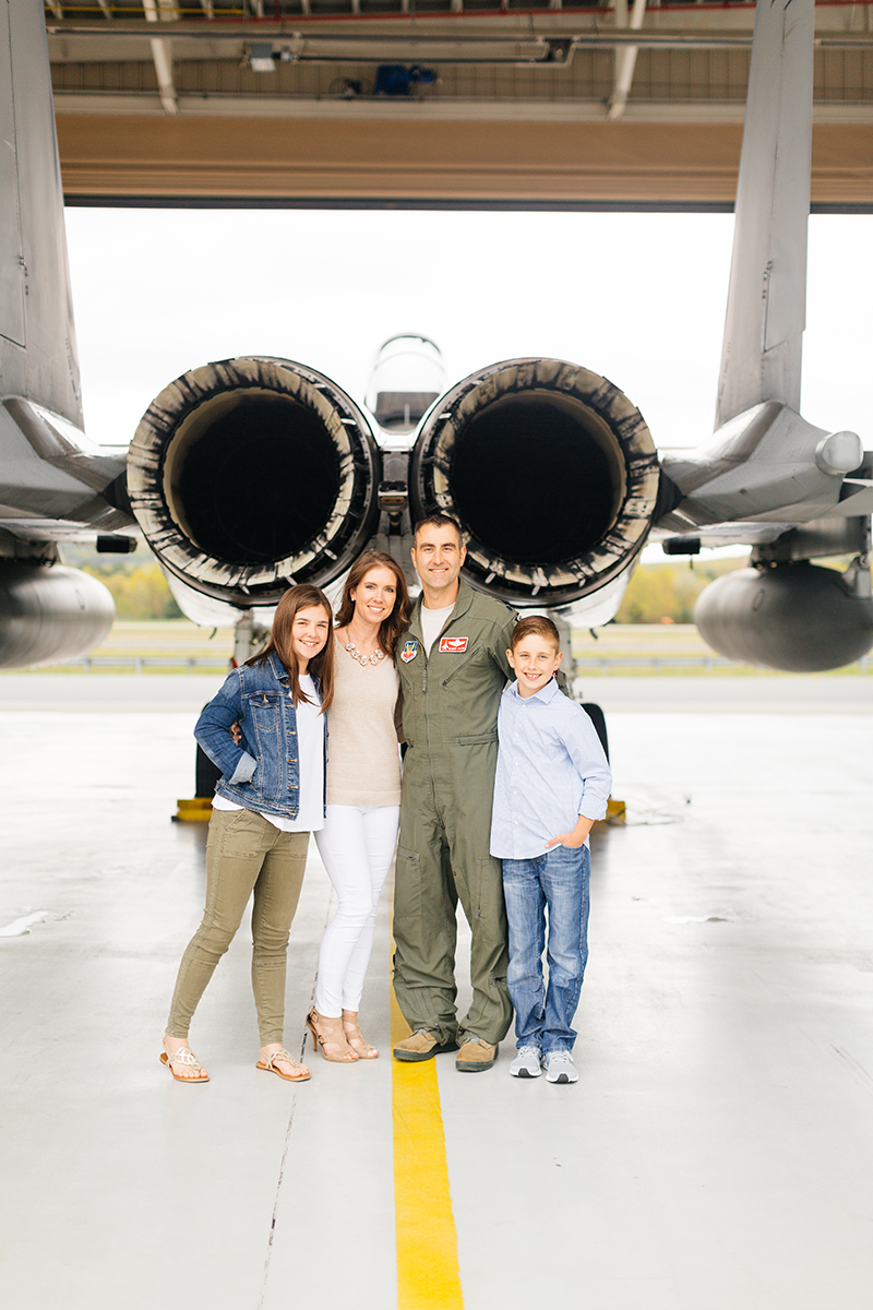 A family stands together behind an F-15 holding each other close at Barnes Air National Guard Base wearing a flight suit and coordinated outfits for these F-15 fighter pilot family photos