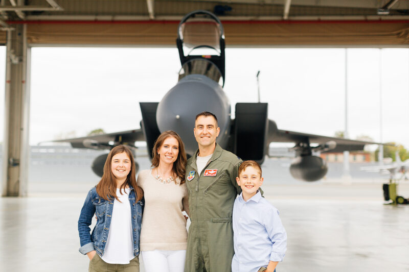 A family stands holding each other close in front of an F-15 at Barnes Air National Guard Base wearing a flight suit and coordinated outfits for these F-15 fighter pilot family photos