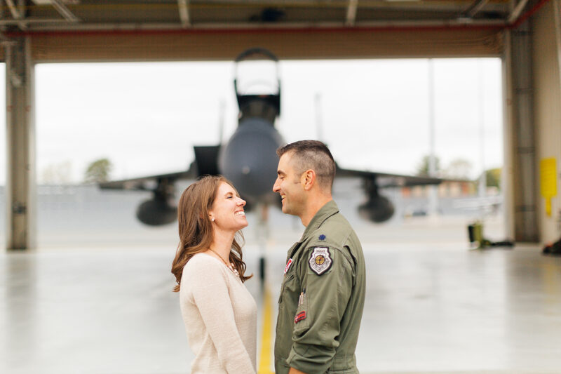 A pilot and his wife stand together in front an F-15 at Barnes Air National Guard Base wearing a flight suit and a coordinated outfit for these F-15 fighter pilot family photos